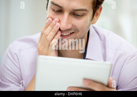 Giovane uomo guardando il messaggio sulla tavoletta digitale Foto Stock