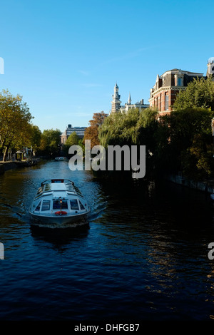 Un tour in barca scivola attraverso un canale d'acqua ad Amsterdam nei Paesi Bassi Foto Stock