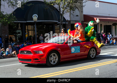 Tre giovani donne e due persone in costumi pappagallo di equitazione in un rosso mustang convertible in UF 2013 Homecoming Parade. Stati Uniti d'America Foto Stock