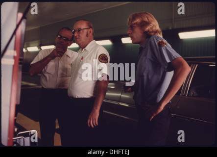 Questa fotografia mostra tre dipendenti del Dipartimento dei lavori pubblici che controllano la lettura di un'auto sottoposta a test su un analizzatore di scarico. La prova fa parte delle misure di controllo delle emissioni del veicolo. Foto Stock