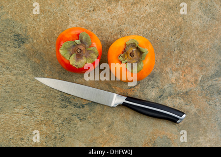 Foto orizzontale di secco fresche Cachi con singolo coltello giacente sulla pietra naturale bancone Foto Stock