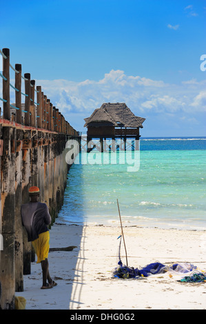 L'uomo la pesca al fianco di un molo hotel, Spiaggia Bwejuu, Oceano Indiano, Zanzibar, Tanzania Africa orientale Foto Stock