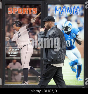 Detroit, Michigan, Stati Uniti d'America. 9 Nov, 2013. Un uomo che indossa un ali rosse di Detroit giacca passeggiate lungo un marciapiede a Detroit il Greektown passato poster di due delle più grandi stelle attualmente in Detroit sport; Tigri slugger Miguel Cabrera e leoni wide receiver Calvin Johnson. Cabrera è ampiamente considerato come il migliore hitter in baseball, e Johnson il miglior ricevitore nel calcio. © Mark Bialek/ZUMAPRESS.com/Alamy Live News Foto Stock