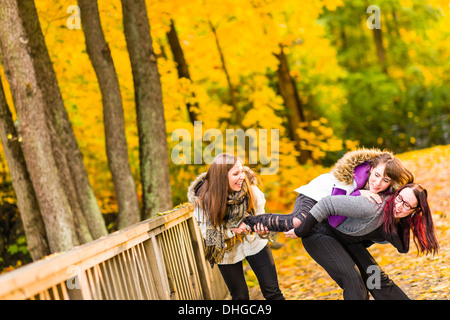 Le tre sorelle giocare scherzi sul ponte e hanno un divertimento insieme sul parco autunnali Foto Stock