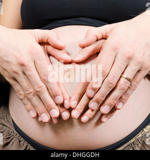 Genitori felici fanno segno di cuore con due coppie di mani sulla donna incinta il ventre Foto Stock