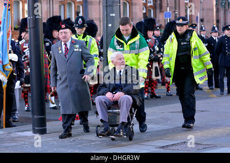 Manchester, Regno Unito. Decimo Nov, 2013. Un uomo anziano è spinto lontano dalla folla dopo il senso di malessere durante il servizio del Ricordo in Piazza San Pietro, Manchester, come i morti di tutte le guerre sono ricordati al 11.00 la domenica più vicina a novembre 11th. Servizio in ricordo di Manchester, UK 10 Novembre 2013 Credit: Giovanni friggitrice/Alamy Live News Foto Stock