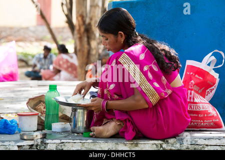 Donna indiana indossando un sari rosa di mangiare un pasto di riso in un villaggio rurale. Andhra Pradesh, India Foto Stock