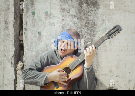 Uomo a suonare la chitarra appoggiata contro la parete Foto Stock