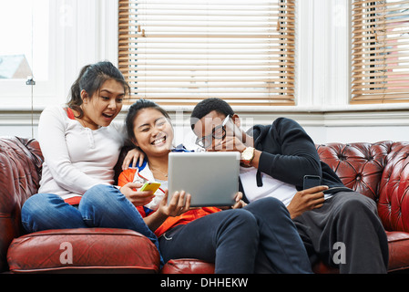 Tre giovani adulti seduti sul divano a ridere a tavoletta digitale Foto Stock