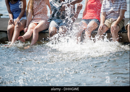 Amici seduti sul molo schizzi a lago Foto Stock