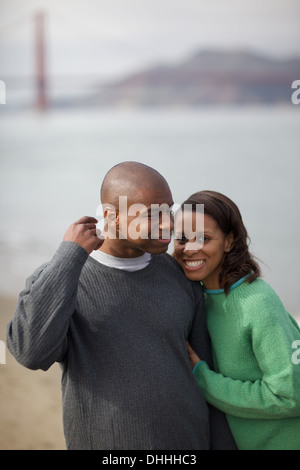 Miscelati calvo e pelose giovane frolic sulla sabbiosa spiaggia sotto lo sguardo di poppa di un fuori fuoco Golden Gate Bridge. Foto Stock
