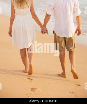 Coppia romantica holding hands camminando sulla spiaggia al tramonto. L uomo e la donna nell'amore. Orme nella sabbia. Foto Stock