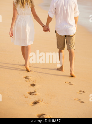 Coppia romantica holding hands camminando sulla spiaggia al tramonto. L uomo e la donna nell'amore. Orme nella sabbia. Foto Stock