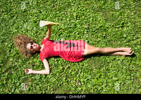 Ragazza adolescente sdraiati sull'erba holding aeroplano di carta Foto Stock