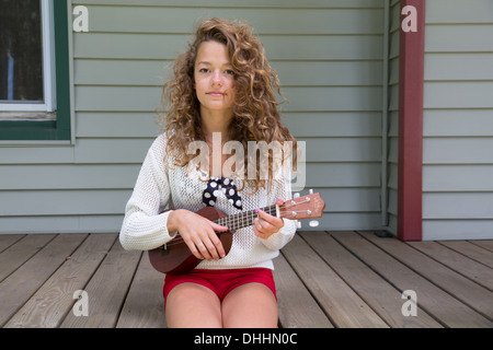 Ragazza seduta sul portico tenendo la chitarra in miniatura Foto Stock