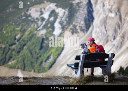 Escursionista seduta su una panchina accanto al suo cane, vicino a Livigno, provincia di Sondrio, Lombardia, Italia Foto Stock