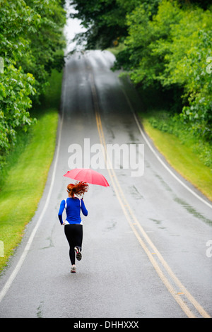 Ragazza adolescente in esecuzione con ombrellone sulla strada, Bainbridge Island, Washington, Stati Uniti d'America Foto Stock