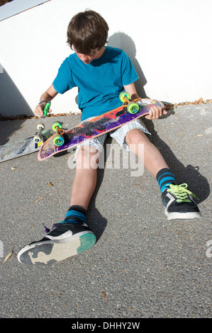 Ragazzo adolescente seduto a terra la preparazione di skateboard Foto Stock