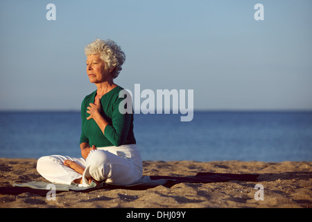 Donna Senior in meditazione da splendido oceano. Eldery donna fare yoga sulla spiaggia. Foto Stock