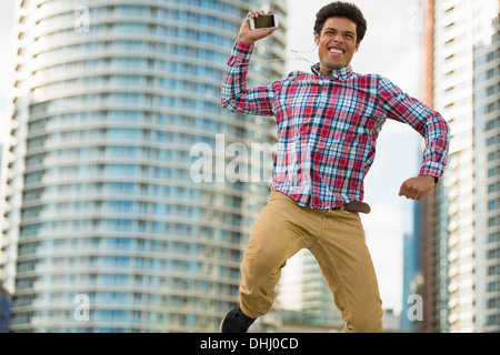 Uomo con telefono cellulare salti di gioia Foto Stock