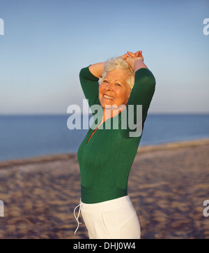 Felice elder donna cercando rilassati sulla spiaggia con le mani sulla sua testa. Attivo femmina senior sulla spiaggia rilassante Foto Stock