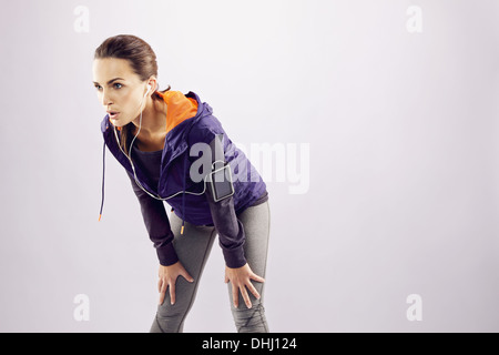 Giovani femmine runner con le mani sulle ginocchia. Stanco giovane donna riposo dopo il jogging su uno sfondo grigio con un sacco di spazio di copia Foto Stock
