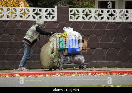 Uomo senza tetto spingendo il carrello con oggetti personali e lattine su strada di città-Victoria, British Columbia, Canada. Foto Stock