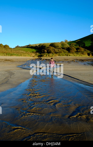 Walker attraversando un allagamento del flusso su di una spiaggia dopo piogge pesanti. Wonwell, South Devon. Regno Unito Foto Stock