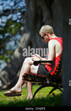 Giovane uomo seduto texting su una panchina nel parco da Mrs Macquarie's Chair, Sydney. Foto Stock