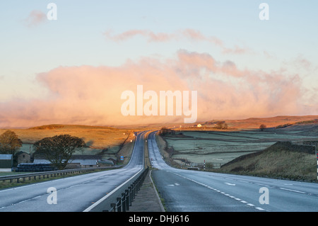 La mattina presto vista lungo un vuoto A66 stradale attraverso Bowes Moor con nuvole all'orizzonte, nell'Inghilterra del Nord, Regno Unito Foto Stock