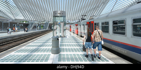 Uomo e donna giovane a piedi tenendo le mani lungo la stazione ferroviaria piattaforma Liegi in Belgio al di sotto di moderna costruzione tetto di vetro soffitto blu cielo estate giorno Foto Stock