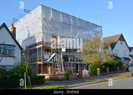 Edilizia cantiere & esistente casa indipendente in impalcatura & protezione telone di plastica durante le modifiche strutturali Essex Inghilterra UK Foto Stock