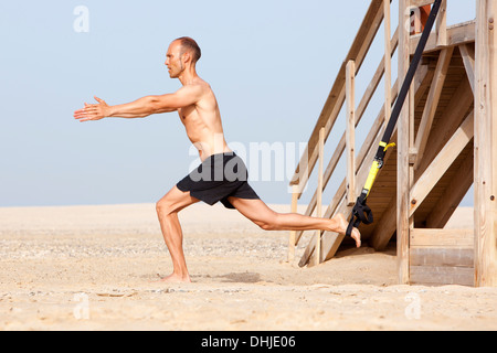 Uomo di sport sulla spiaggia con trx Foto Stock