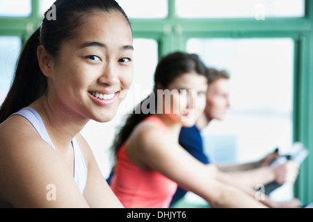 Le giovani donne che esercitano sulla bici fitness in palestra, guardando la fotocamera Foto Stock