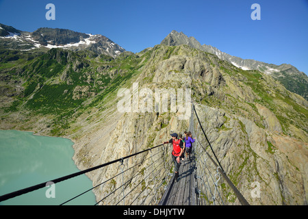 Gli escursionisti a piedi su un ponte di sospensione su un lago di montagna, Trift glacier, Trift ponte di sospensione, Tieralplistock, Urner Al Foto Stock