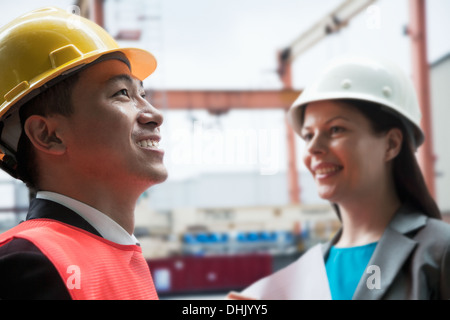 Due ingegneri sorridente in indumenti da lavoro protettiva al di fuori in un cantiere di spedizione Foto Stock