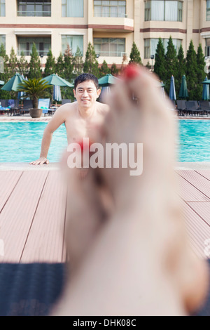 Close up della giovane donna di piedi dal bordo della piscina, l'uomo in uscita dell'acqua in background Foto Stock