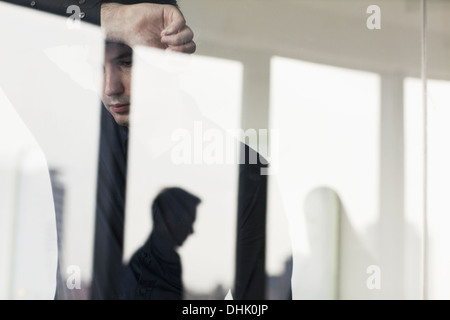 Imprenditore oberato di lavoro con il braccio sollevato appoggiata sull'altro lato di una parete di vetro Foto Stock