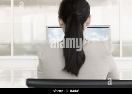 Imprenditrice seduto davanti a un computer con le nuvole e il cielo sul monitor Foto Stock