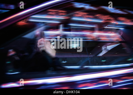 Imprenditore guidare di notte, illuminato e luci riflesse sul vetro dell'auto Foto Stock