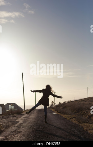 Silhouette di una ragazza facendo un salto a stella su una strada remota nelle Highlands Scozzesi. Foto Stock