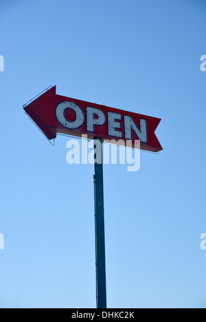 Neon vecchio segno aperto conformato come una freccia, rosso sbiadito e contro un cielo blu Foto Stock