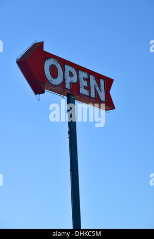 Neon vecchio segno aperto conformato come una freccia, rosso sbiadito e contro un cielo blu Foto Stock