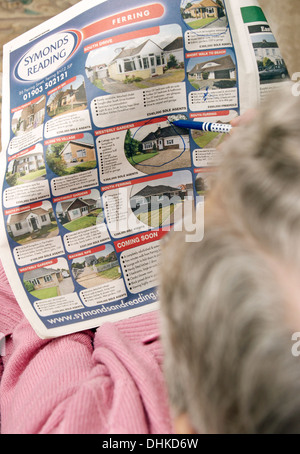 Donna anziana guardando le proprietà sulla pagine delle proprietà in un giornale locale & marcatura fuori qualcosa di interessante Foto Stock