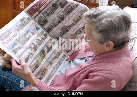 Donna anziana guardando le proprietà sulla pagine delle proprietà in un giornale locale Foto Stock