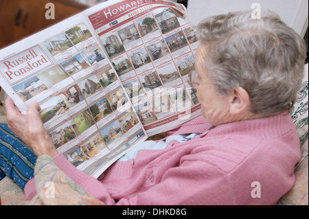 Donna anziana guardando le proprietà sulla pagine delle proprietà in un giornale locale Foto Stock