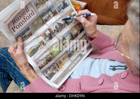 Donna anziana guardando le proprietà sulla pagine delle proprietà in un giornale locale & marcatura fuori qualcosa di interessante Foto Stock