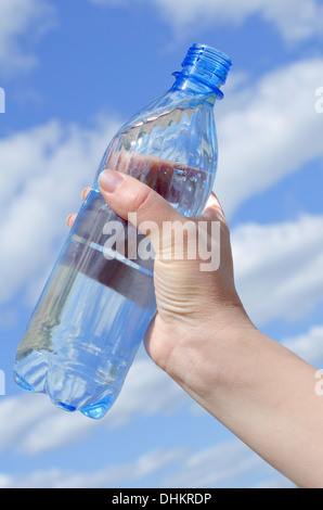 Acqua in bottiglia in una mano contro il cielo Foto Stock