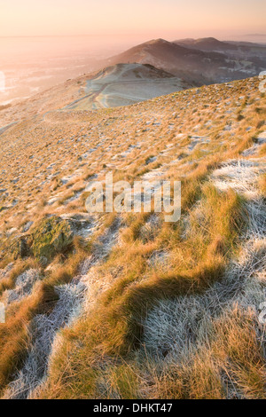 Sole sorge su Malvern Hills colata di ombre e punti di luce sul frosted ciuffi di erba sui Worcestershire Beacon. Foto Stock