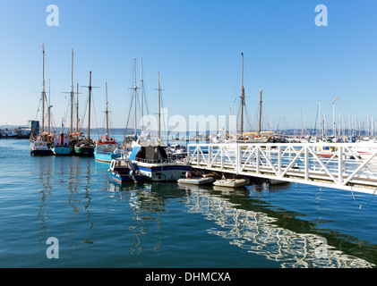 Pontile bianco passerella che conduce a barche e yacht in un marina con cielo blu e riflessi Foto Stock